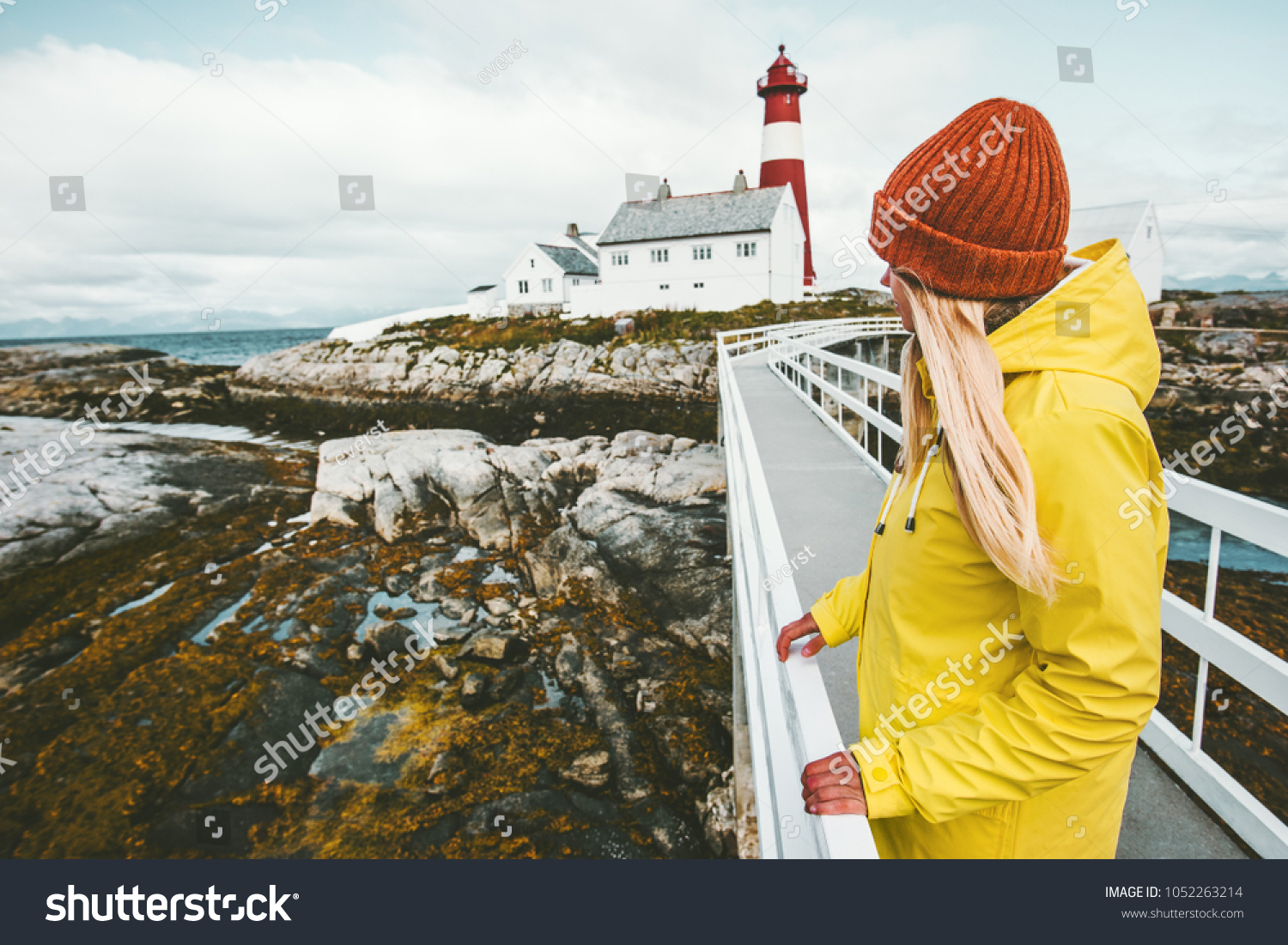 Woman sightseeing Norway lighthouse landscape Travel Lifestyle concept adventure tourist at vacations outdoor girl wearing yellow raincoat standing alone #1052263214