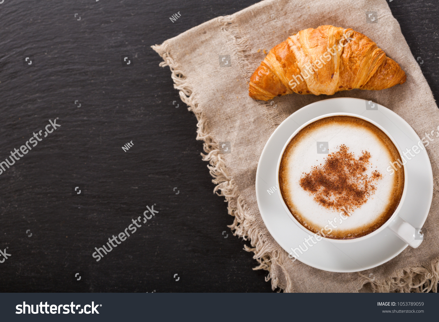 Cup of cappuccino coffee and croissant on dark table, top view #1053789059