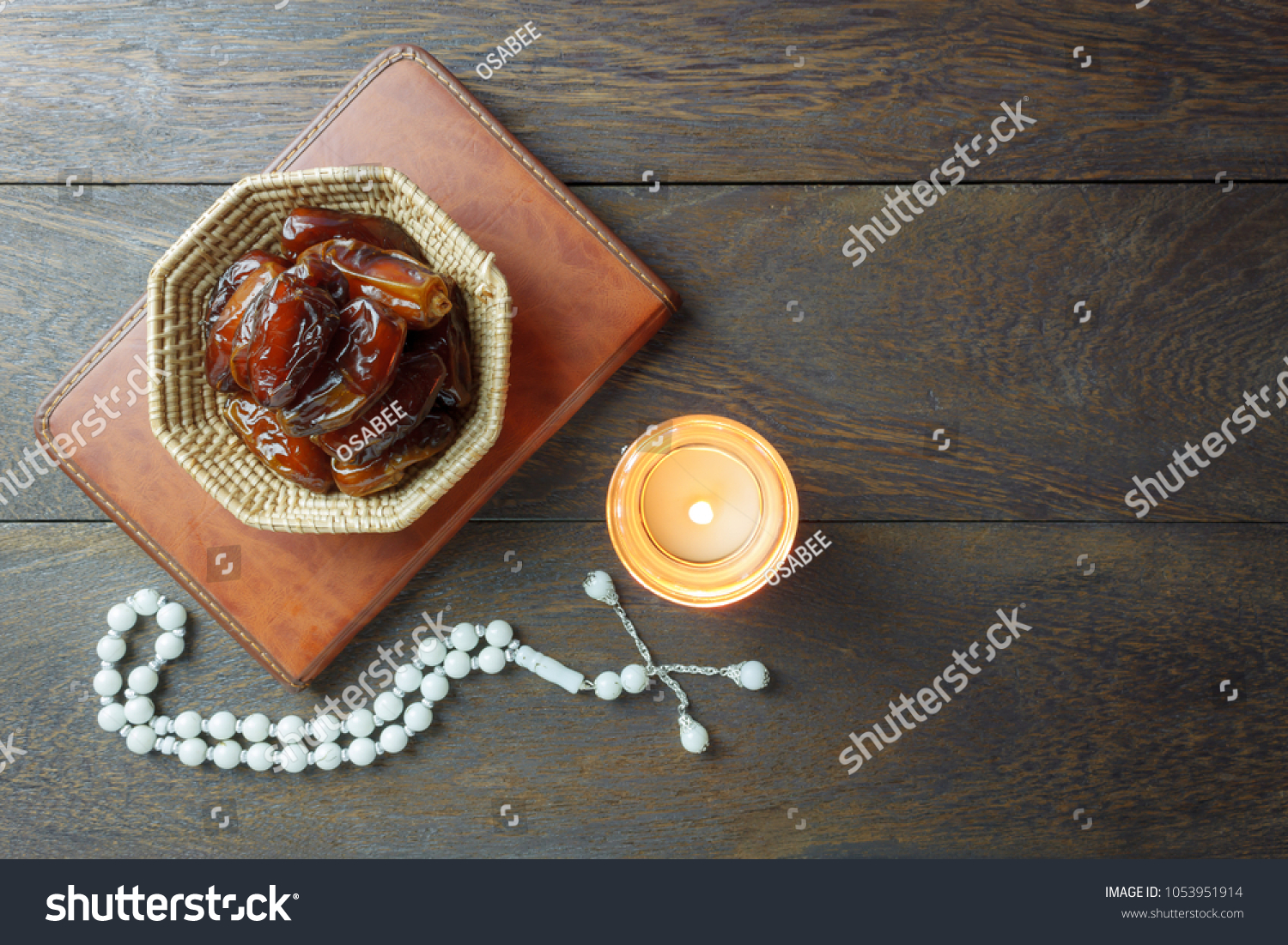 Table top view aerial image of decoration Ramadan Kareem holiday background.Flat lay date in wood basket with white rosary & lighting.The holy book of Koran on modern rustic brown wood at office desk. #1053951914