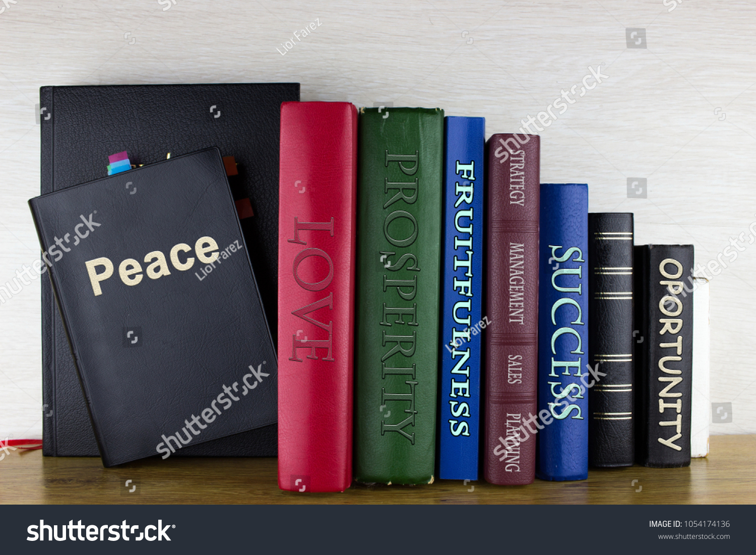 Set of books on a wooden shelf with written titles: Peace, Love, prosperity, fruitfulness, management, success, opportunity, strategy, planning. #1054174136