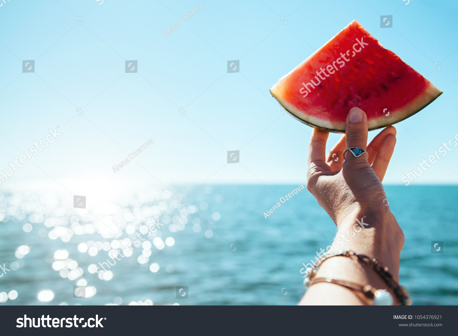 Watermelon slice in woman hand over sea - POV. Summer beach concept. Tropical fruit diet. #1054376921