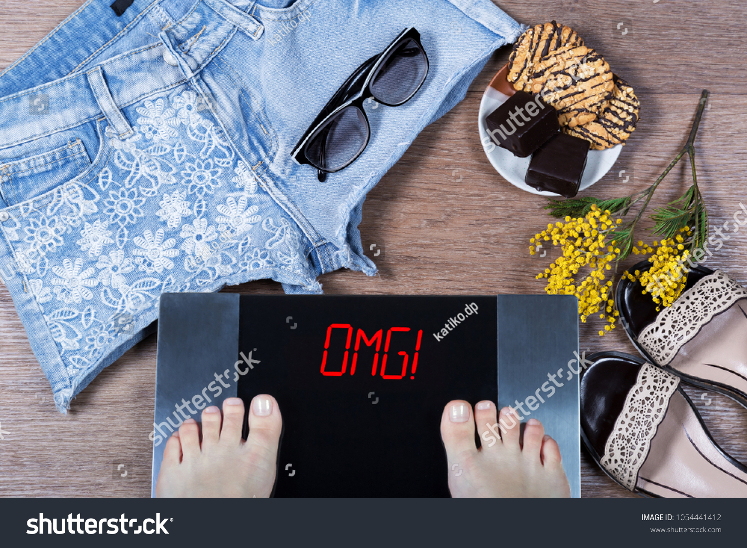 Digital scales with female feet and sign omg! surrounded by mimosa flowers, shorts and sweets. Effect of unhealthy food at body. Concept of being in form before spring and summer. Top view. Flat lay. #1054441412