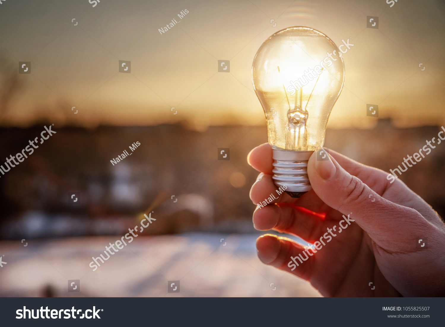 Light bulb in hand on the rising sun background. #1055825507