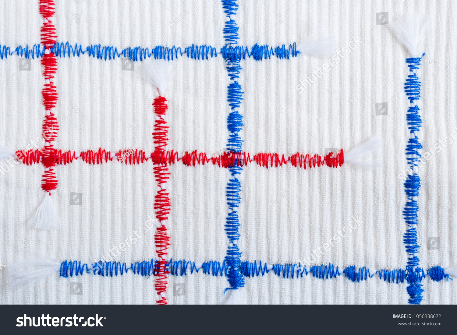 Close-up randomly arranged vertical and horizontal red and blue textural  zigzag seams on relief white fabric. #1056338672