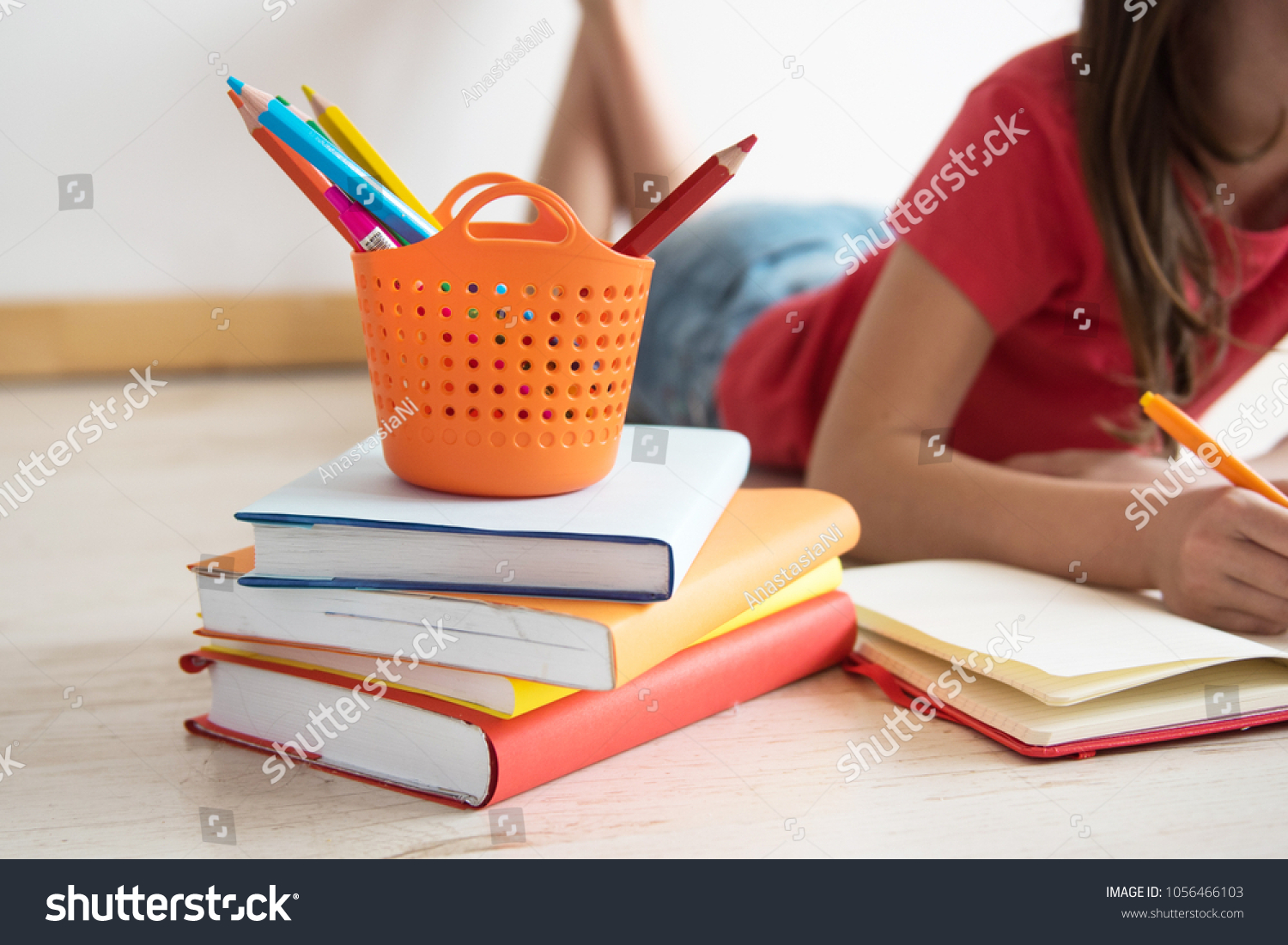 Homeschooling. The child, the pupil, the schoolgirl lies on a floor with a pile of books and writes homework. Education of children. Training of children in kindergartens and schools. #1056466103