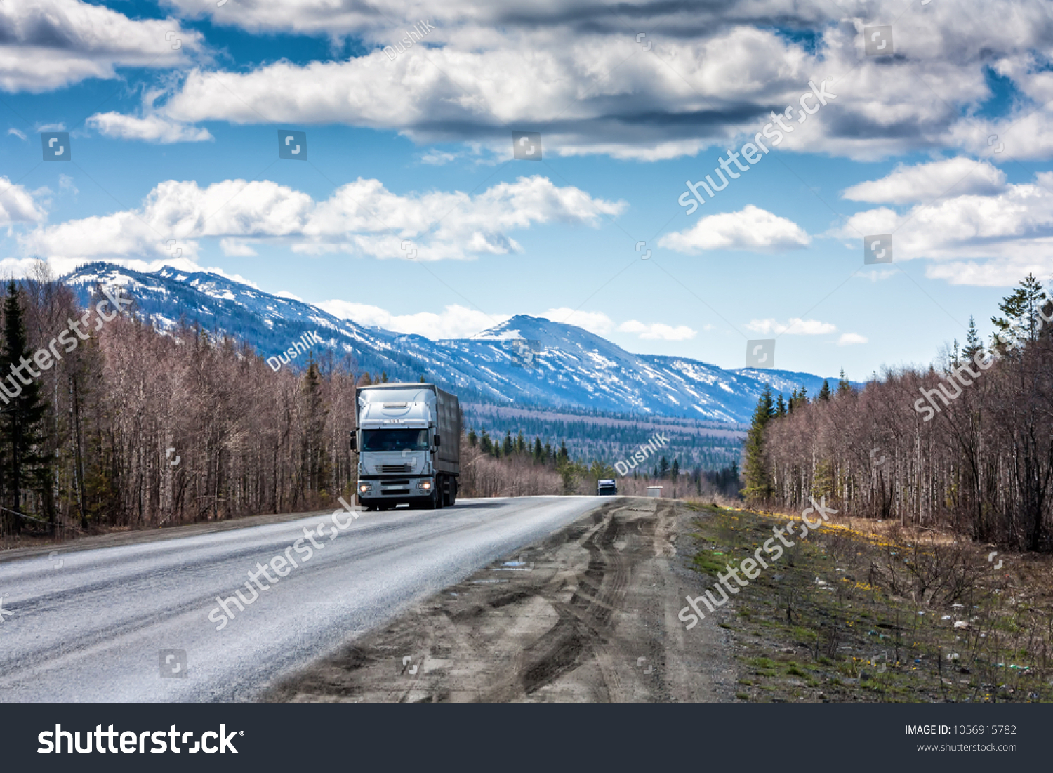 A long-distance truck with a semitrailer moves on the road among the mountains covered with snow #1056915782