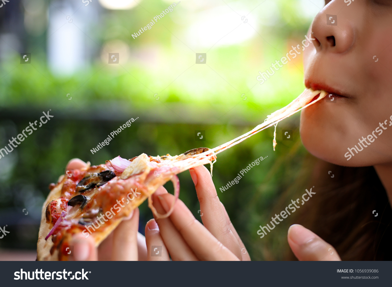 Pizza look so yummy or delicious food. Charming beautiful asia woman is eating pepperoni pizza and sticky mozzarella cheese. Attractive girl feels hungry and loves the taste. She sit at restaurant #1056939086