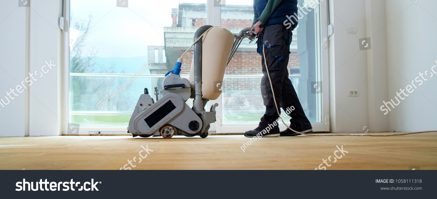 Sanding hardwood floor with the grinding machine. Repair in the apartment. Carpenter doing parquet wood floor polishing maintenance work by grinding machine #1058111318