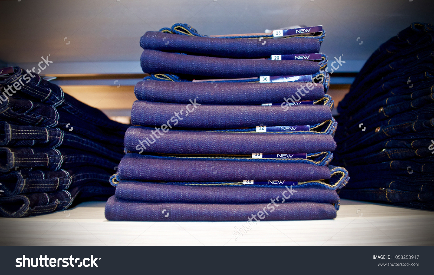 Stacked of folded jeans in store on wooden shelf. #1058253947