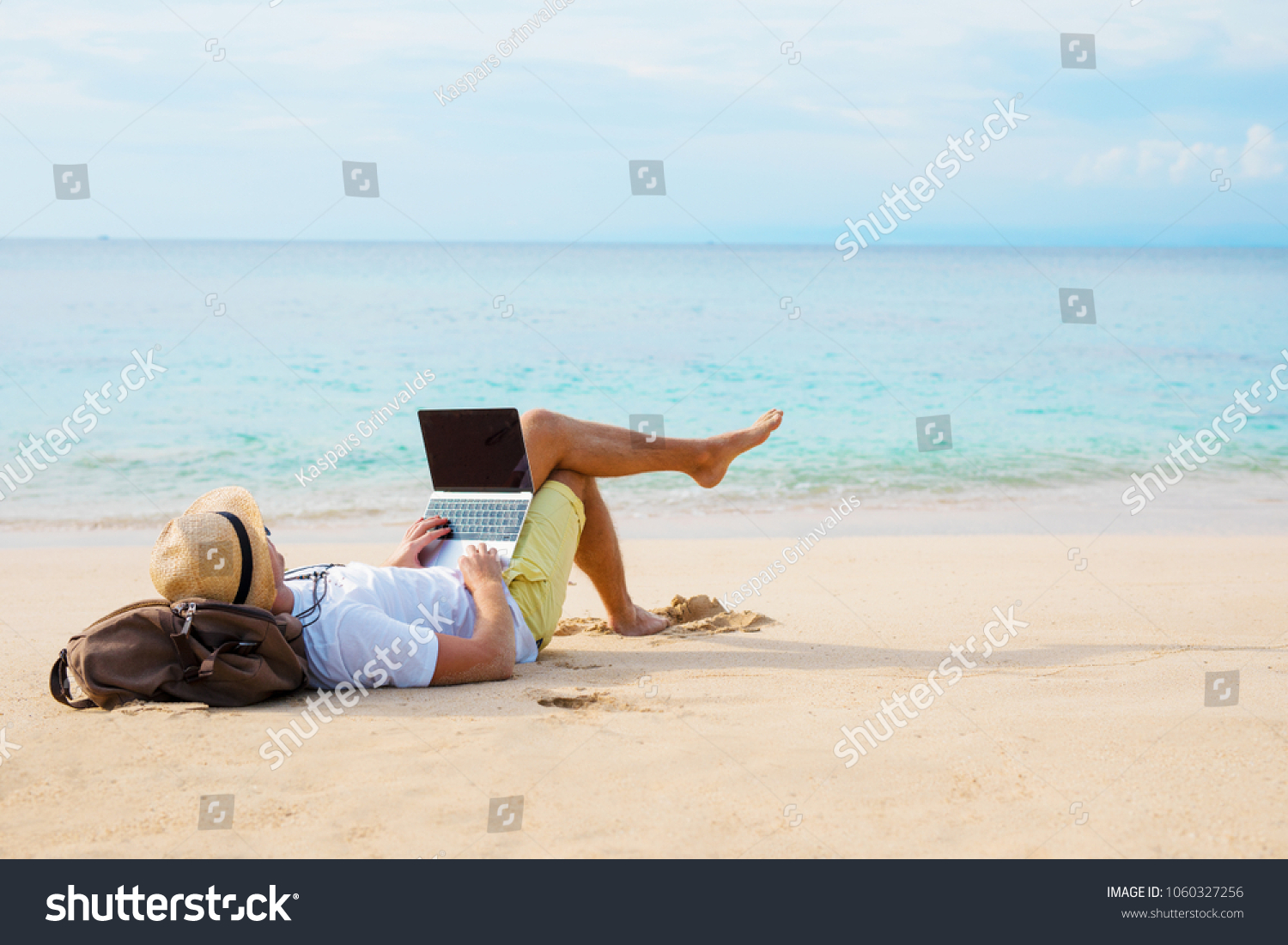 Man working on laptop computer while relaxing on the beach #1060327256