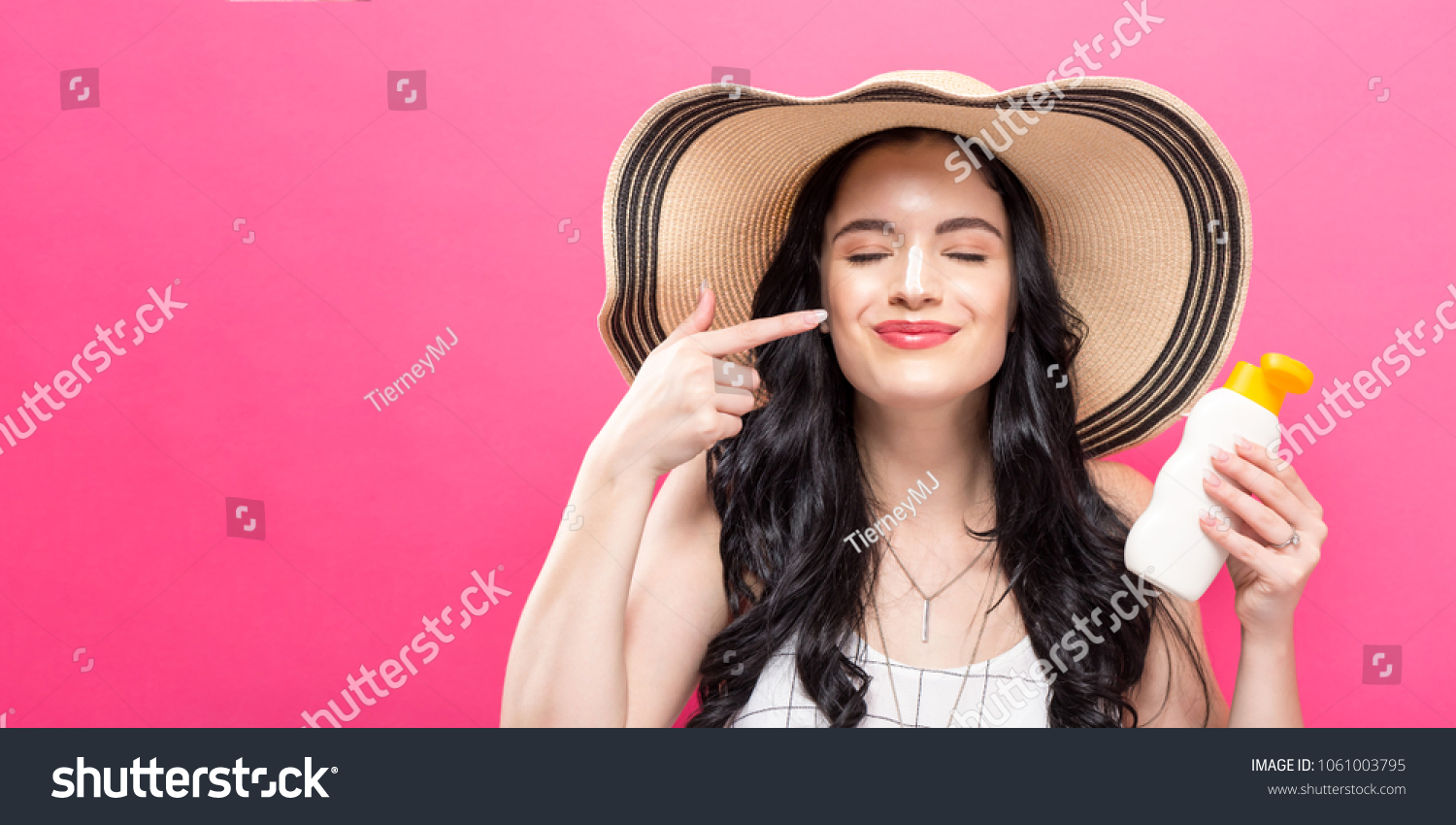 Young woman holding a bottle of sunblock on a solid background #1061003795
