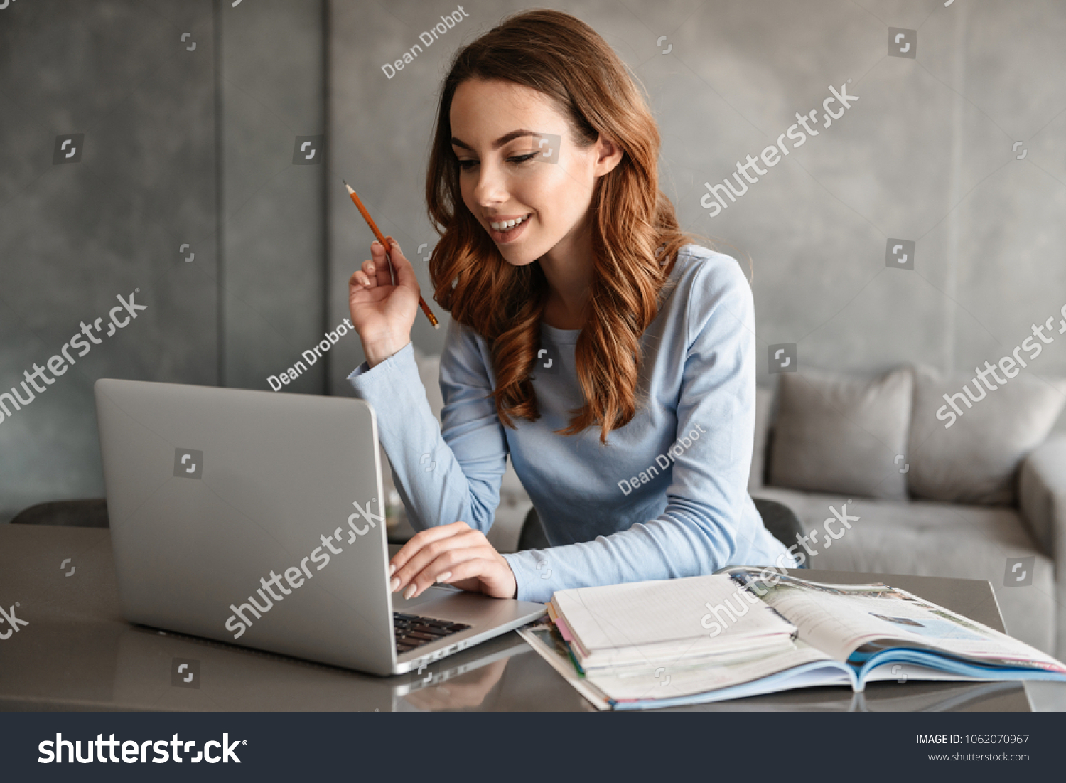 Portrait of a pretty young woman studying while sitting at the table with laptop computer and notebook at home #1062070967