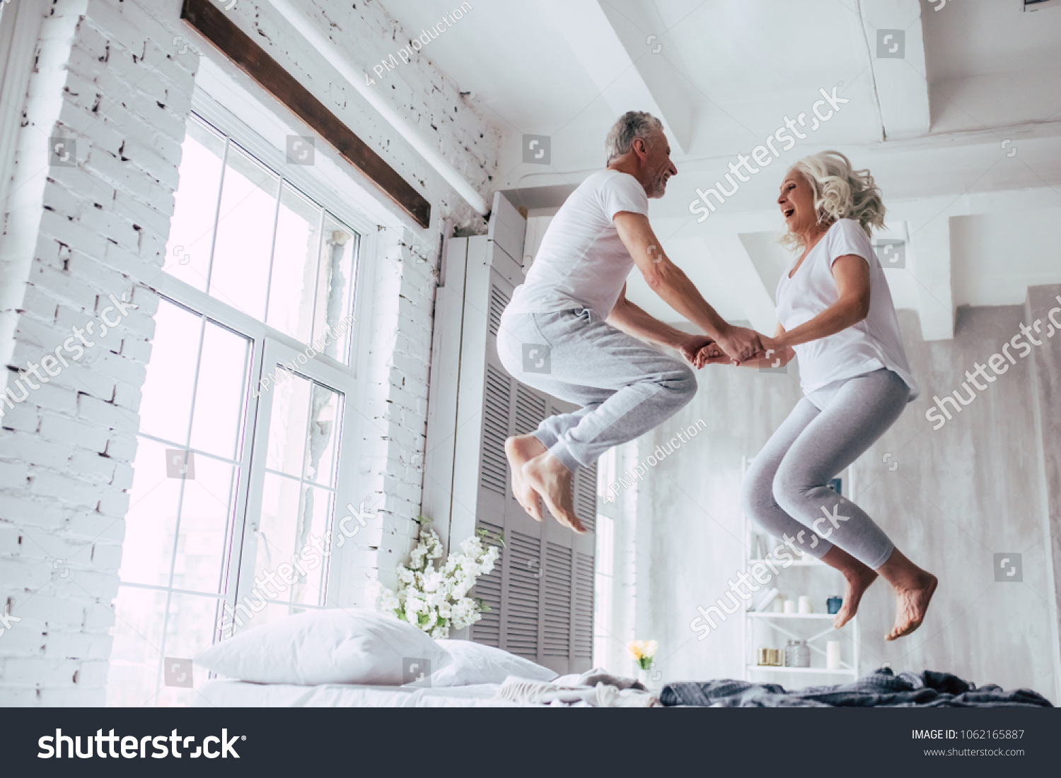 Love lives forever! Senior couple at home. Handsome old man and attractive old woman are enjoying spending time together. Having fun and jumping in bed. #1062165887