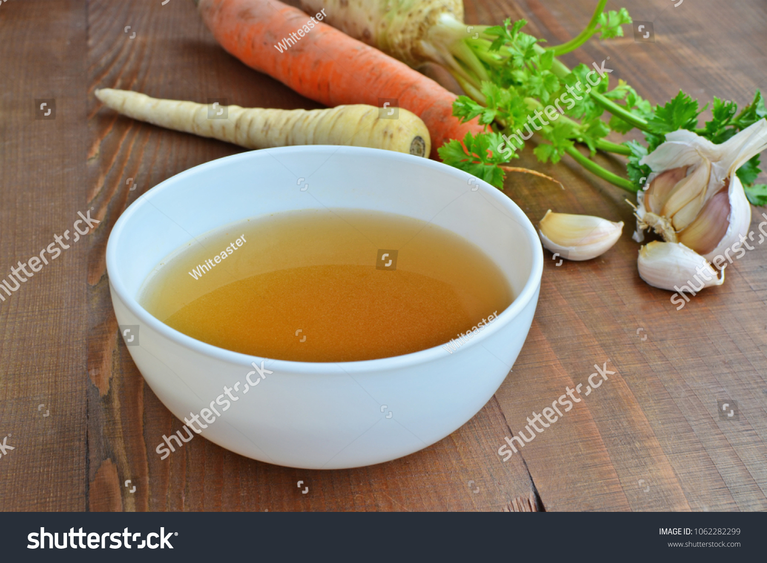 Clear beef broth, bone broth, bouillon in white bowl and vegetables on wooden table  #1062282299