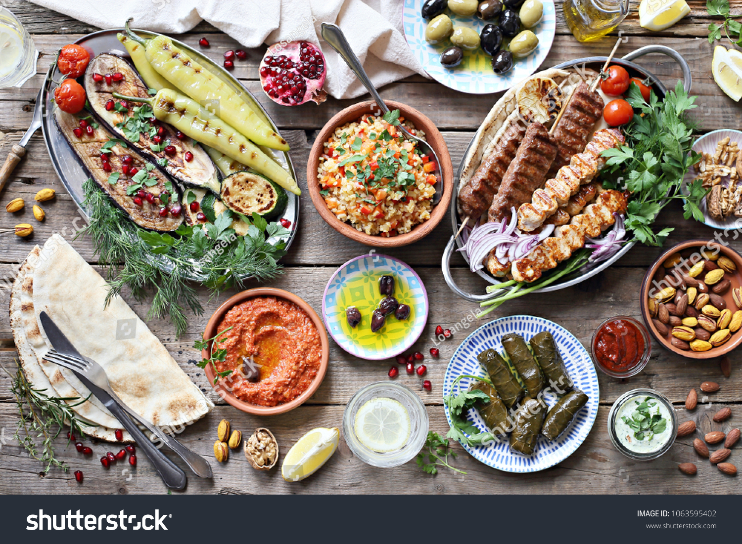 Middle eastern, arabic or mediterranean dinner table with grilled lamb kebab, chicken skewers  with roasted vegetables and appetizers variety serving on rustic outdoor table. Overhead view. #1063595402