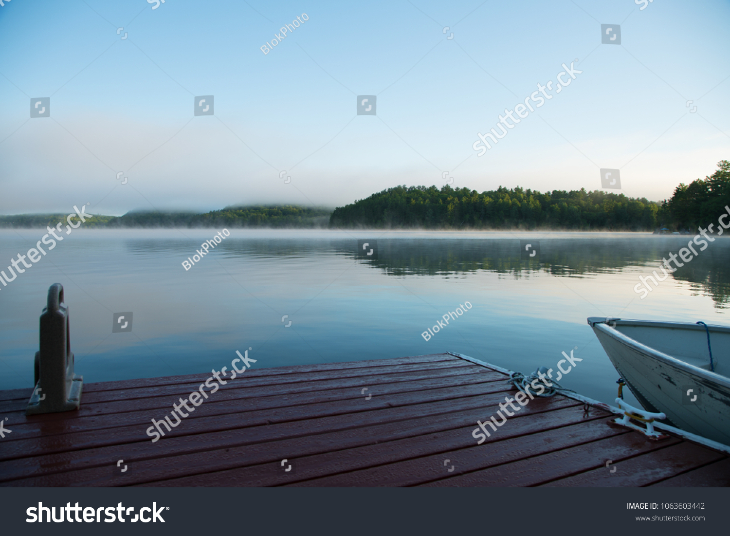 A lakeside dock and fishing boat on an Ontario lake in the morning mist #1063603442