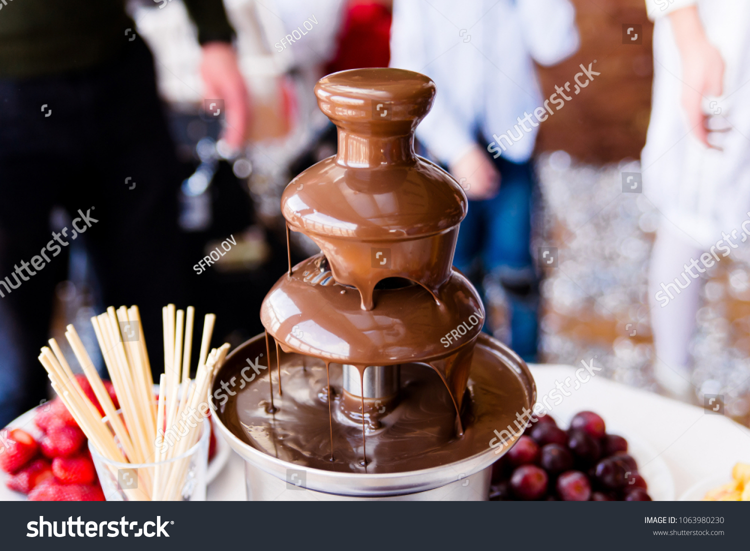 Vibrant Picture of Chocolate Fountain Fontain on childen kids birthday party with a kids playing around and marshmallows and fruits dip dipping into fountain #1063980230