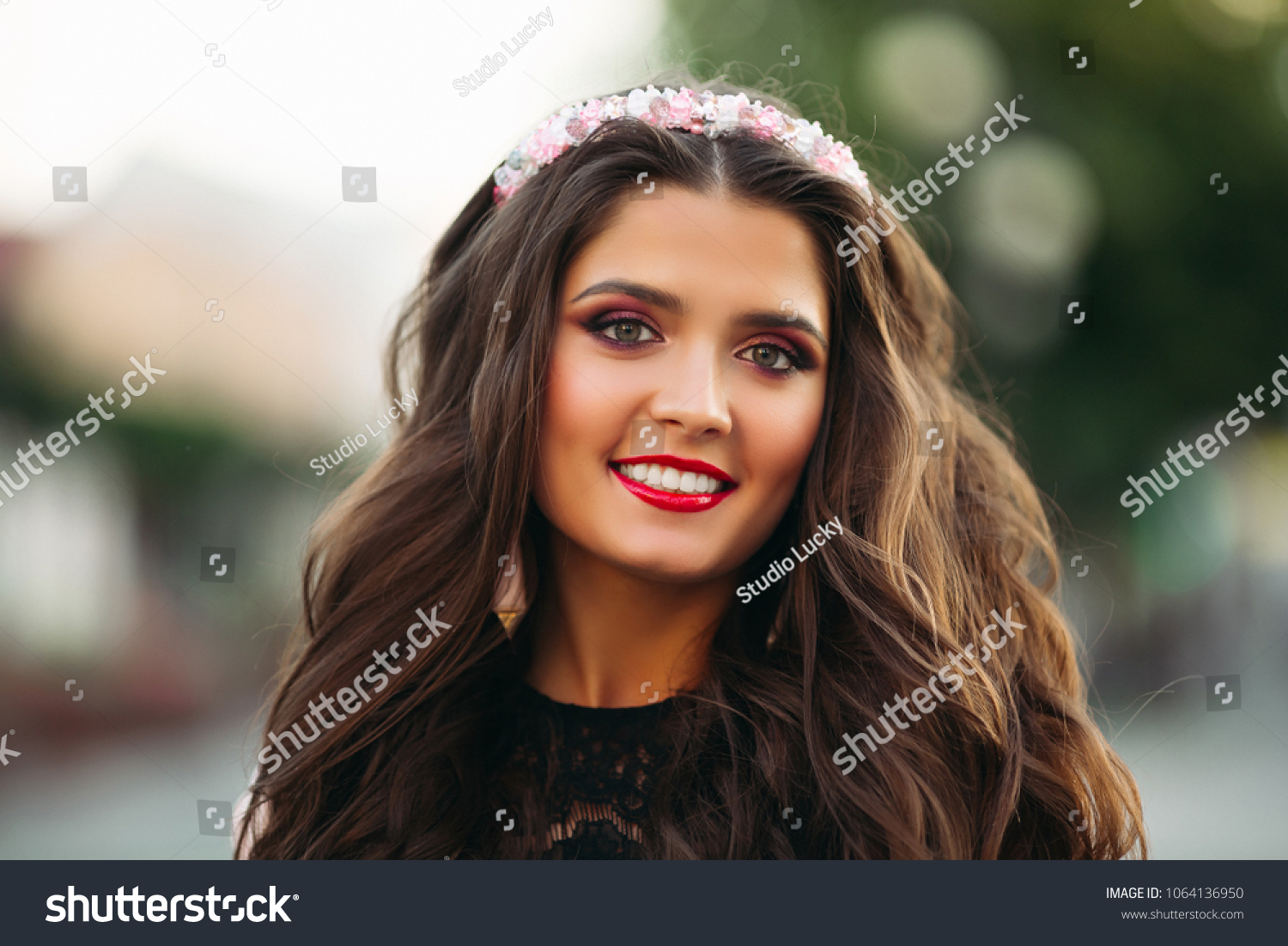 Portrait of beauty brunette with make up wearing flower diadem smiling at camera over blurred background. #1064136950