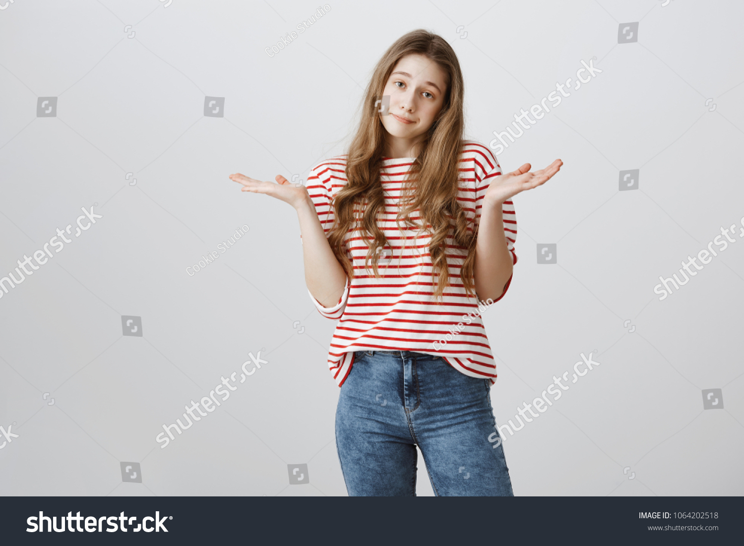 I do not care about rules. Portrait of indifferent careless teenage girl with blonde hair shrugging and holding spread palms near shoulders, being uninterested and bothered with stupid questions #1064202518