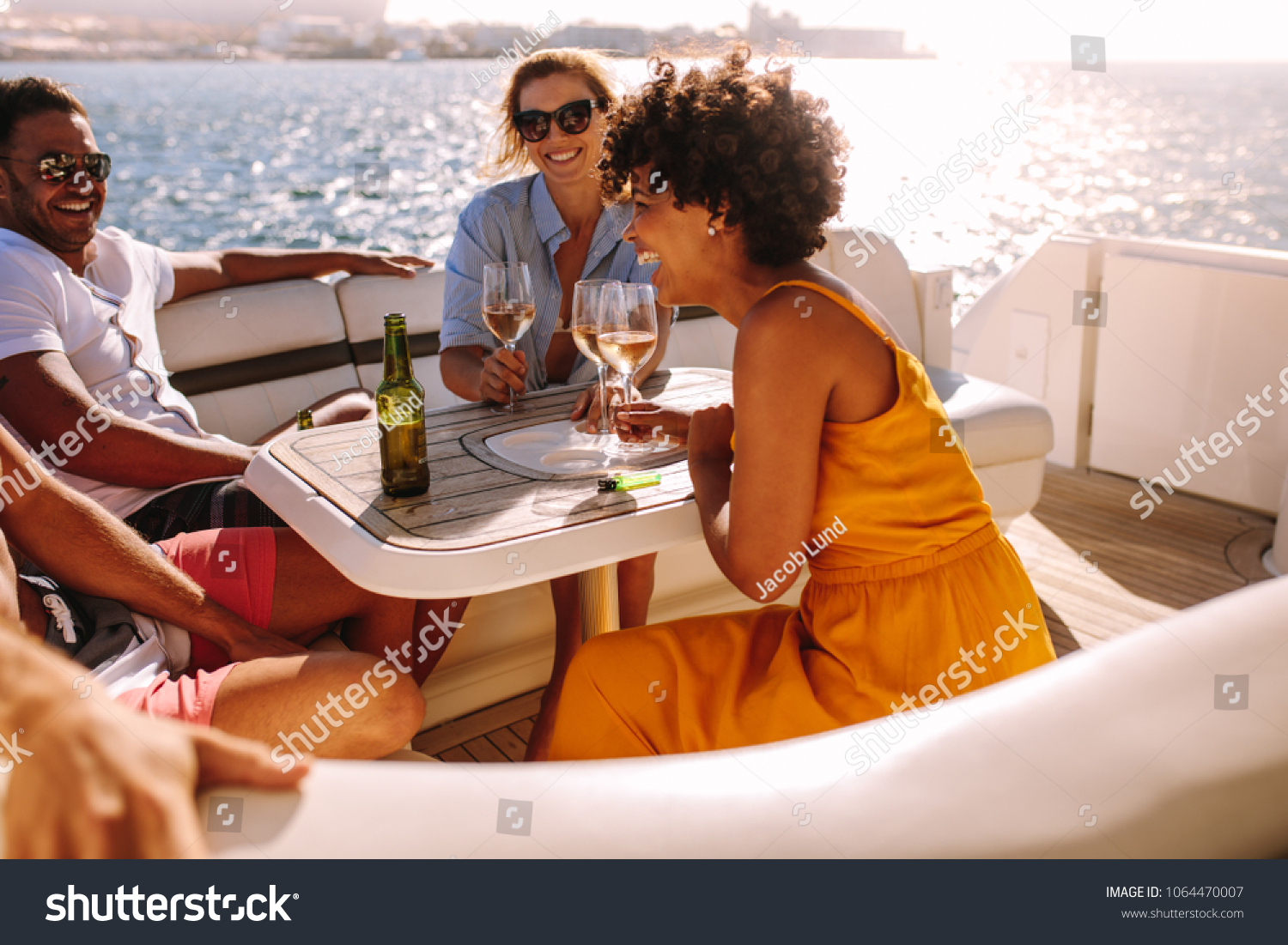 Group of young people having a boat party. Friends sitting at the back of a yacht and partying. #1064470007