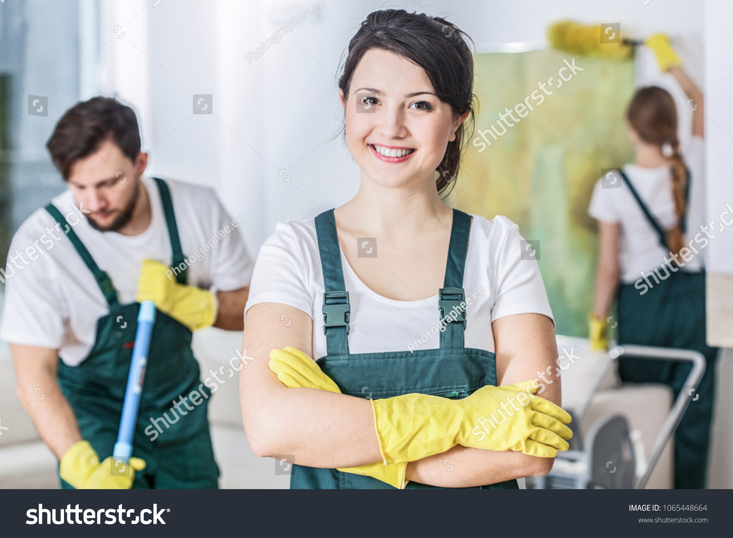 Smiling cleaning lady in a green uniform and yellow rubber gloves at work #1065448664