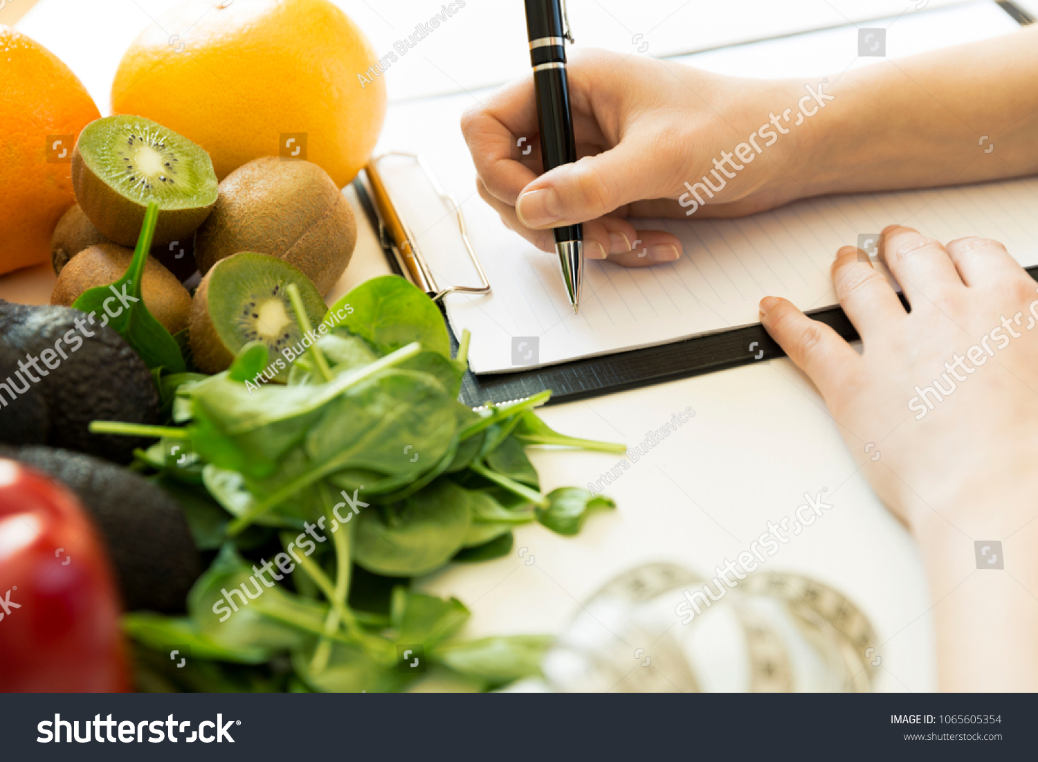 Nutritionist woman writing diet plan on table full of fruits and vegetables #1065605354