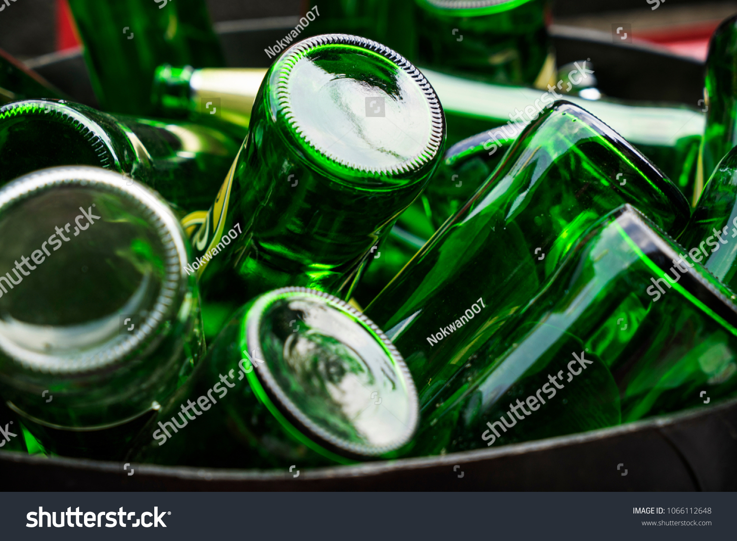 Pile of empty beer, green glass bottles, invert bottom up collected in steel bin for recycle selling. Container industry or waste management concept. #1066112648