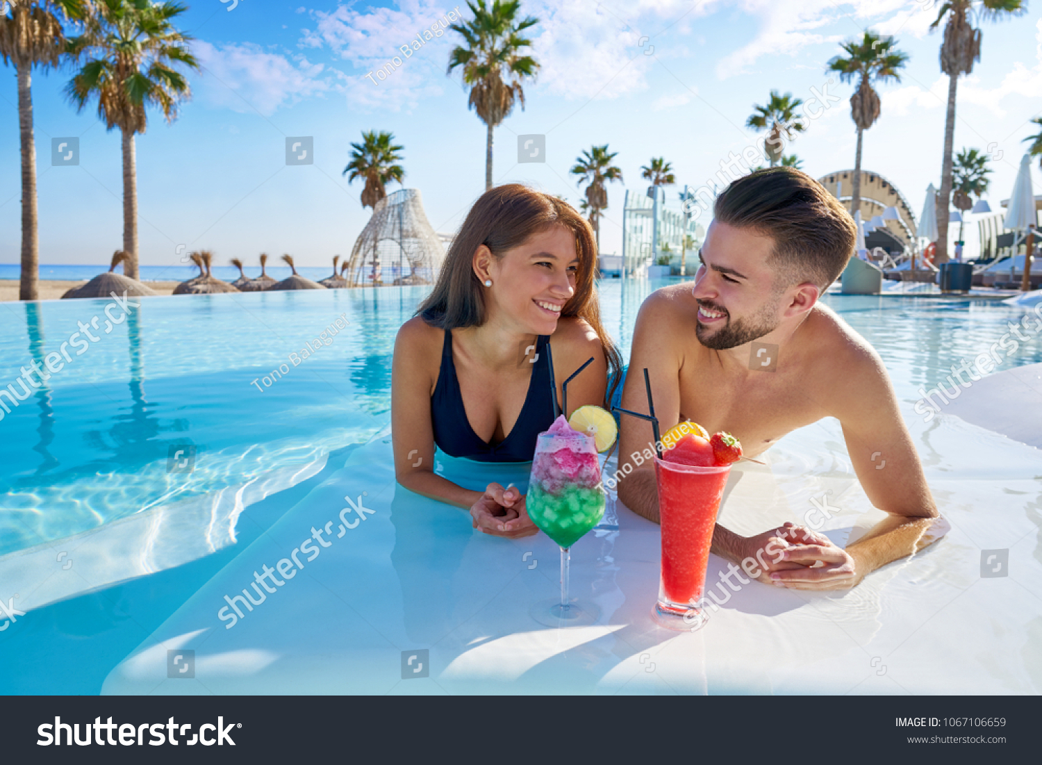Young tourist couple on infinity pool drinking cocktails at resort on the beach #1067106659