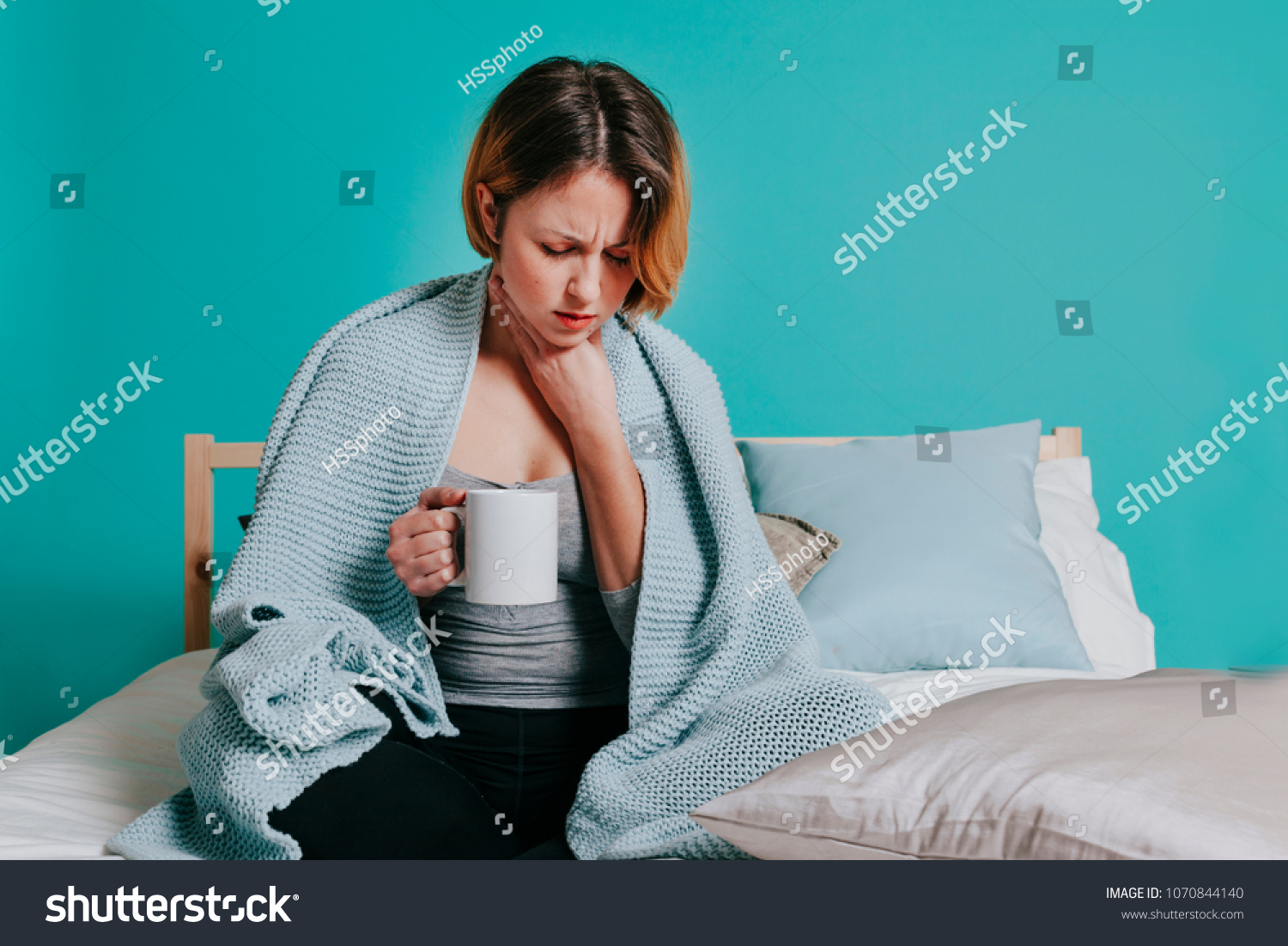 Woman sore throat with glass of water in her bed. Blue background #1070844140