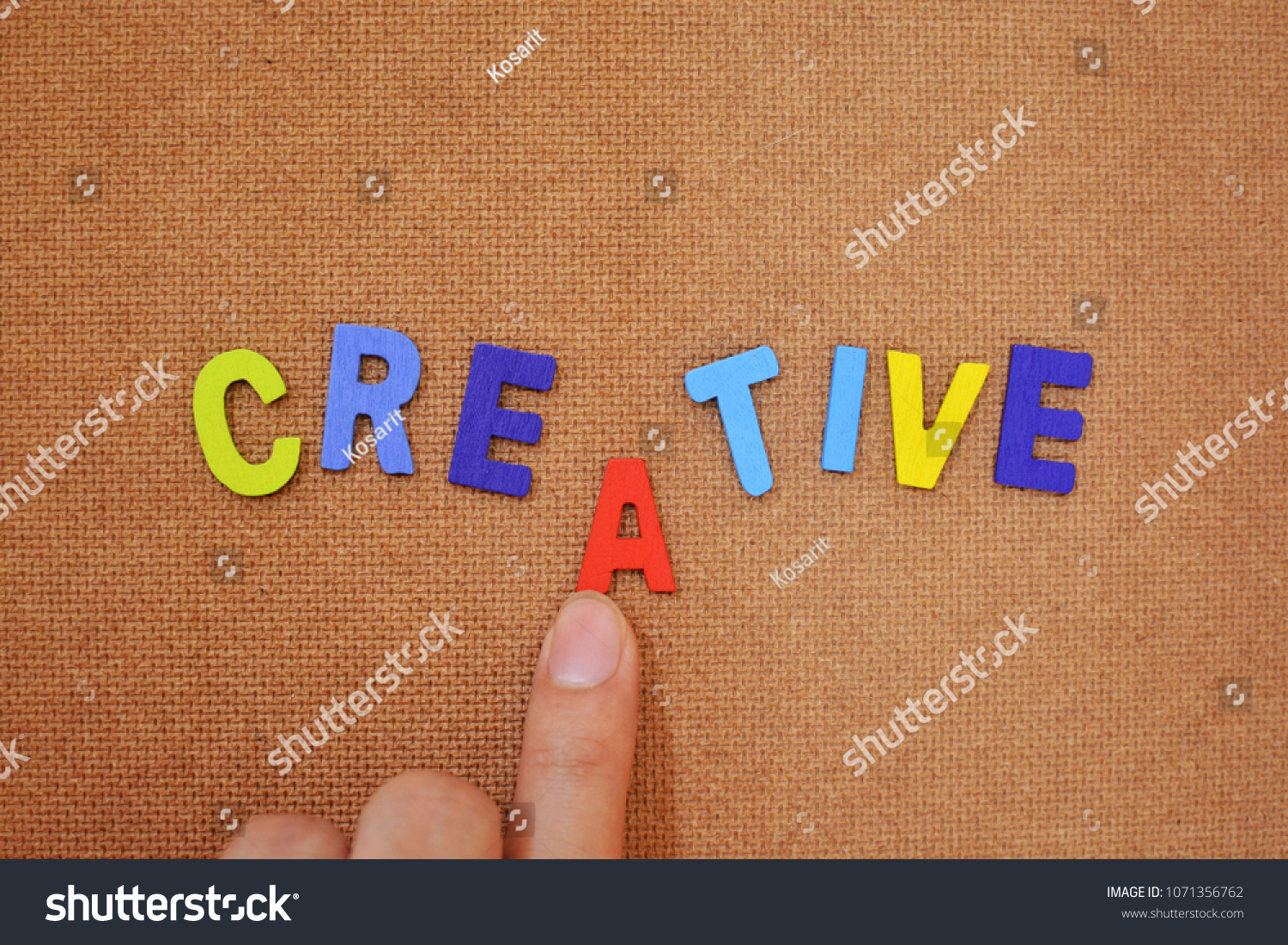 Colorful words concept. The word “creative” on brown plywood background. A finger pushing an alphabet to complete the word. #1071356762