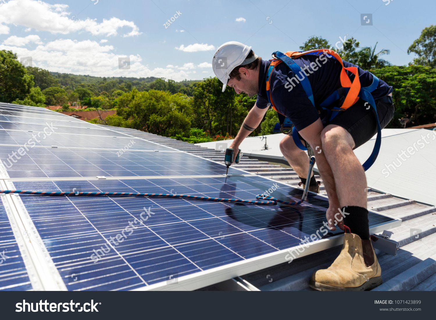 Solar panel technician with drill installing solar panels on roof on a sunny day #1071423899