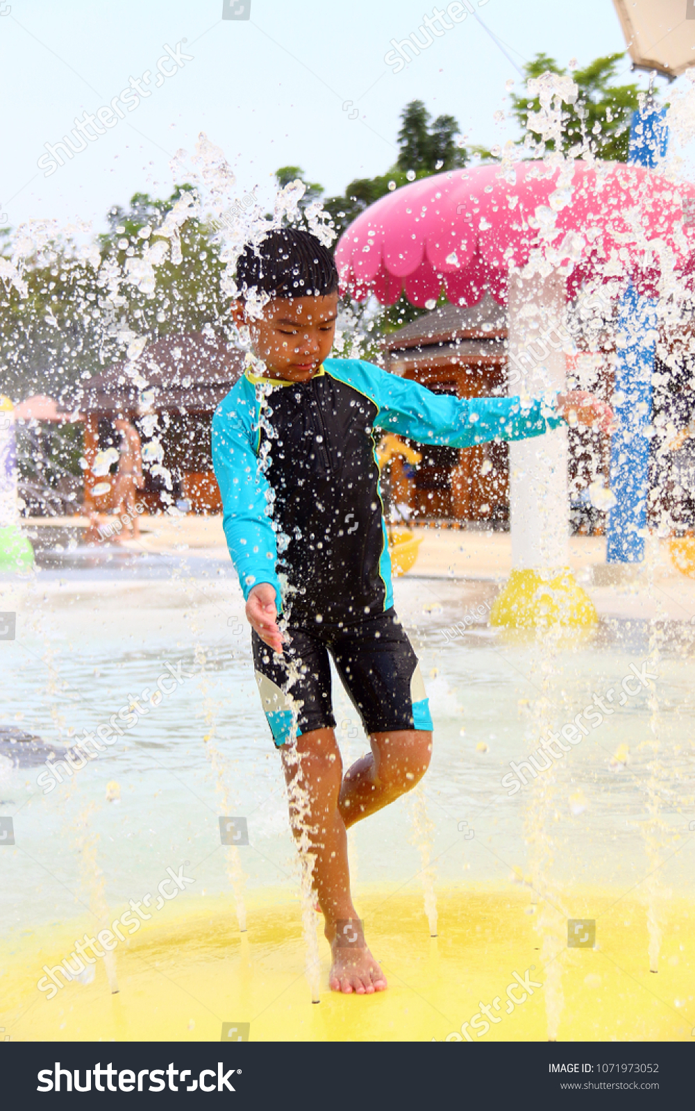 A boy wearing a swimsuit is playing splashing water. #1071973052