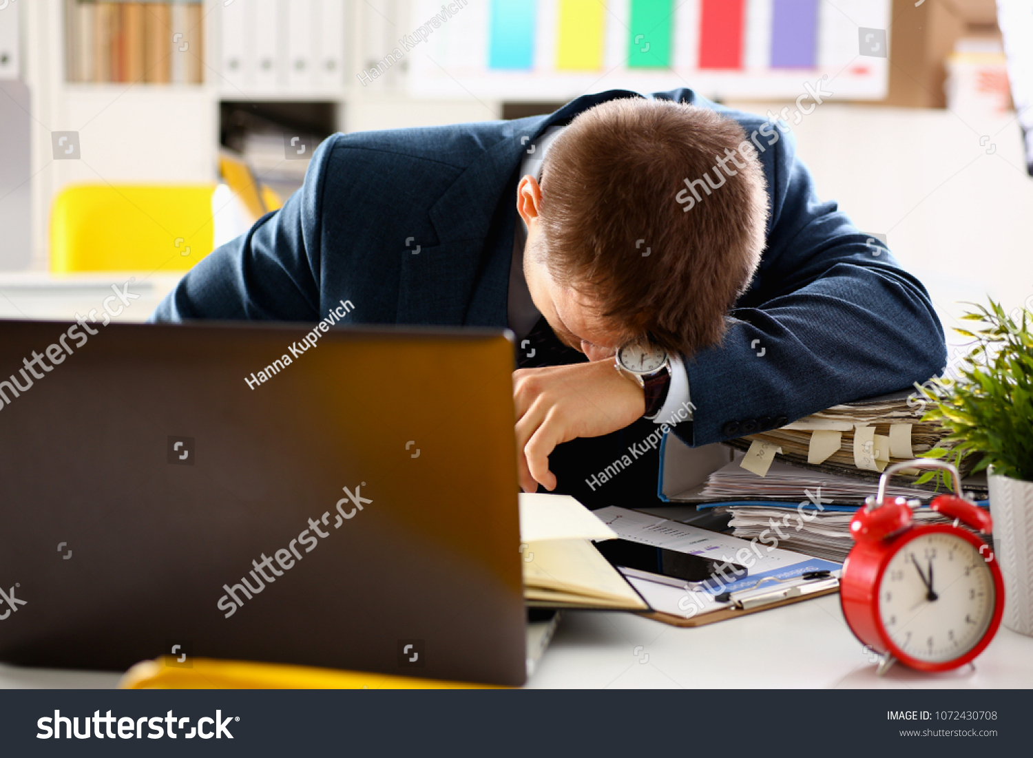 Red alarm clock shows late time closeup and tired office male clerk in suit take nap on table workplace full of exam papers. Career frustration freelance employment fail study problem low energy down #1072430708