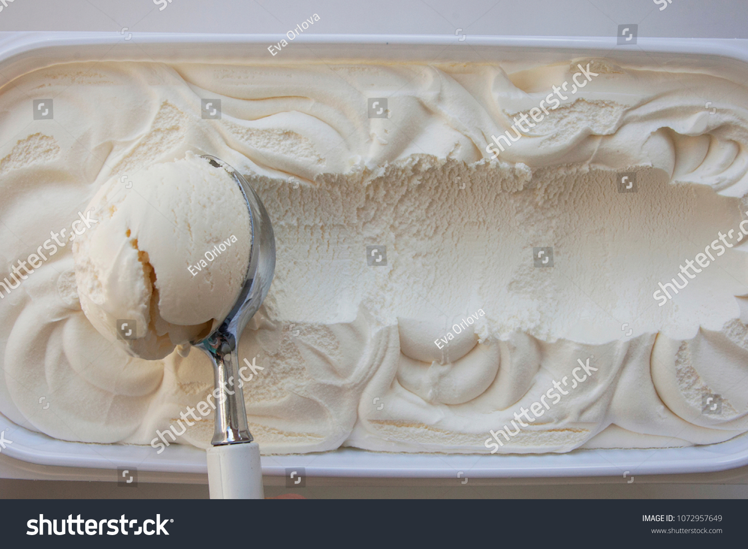 Vanilla ice cream Flat lay. Top view. Spoon for ice cream takes a little out of the package. Macking ball of ice cream. Space for text. #1072957649
