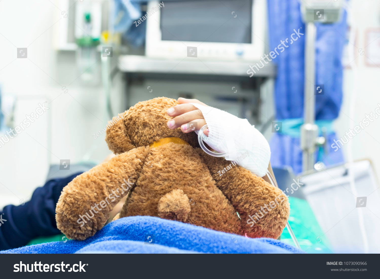 The girl was given intravenous fluid hugging a teddy bear while lying in the emergency room of the hospital. #1073090966