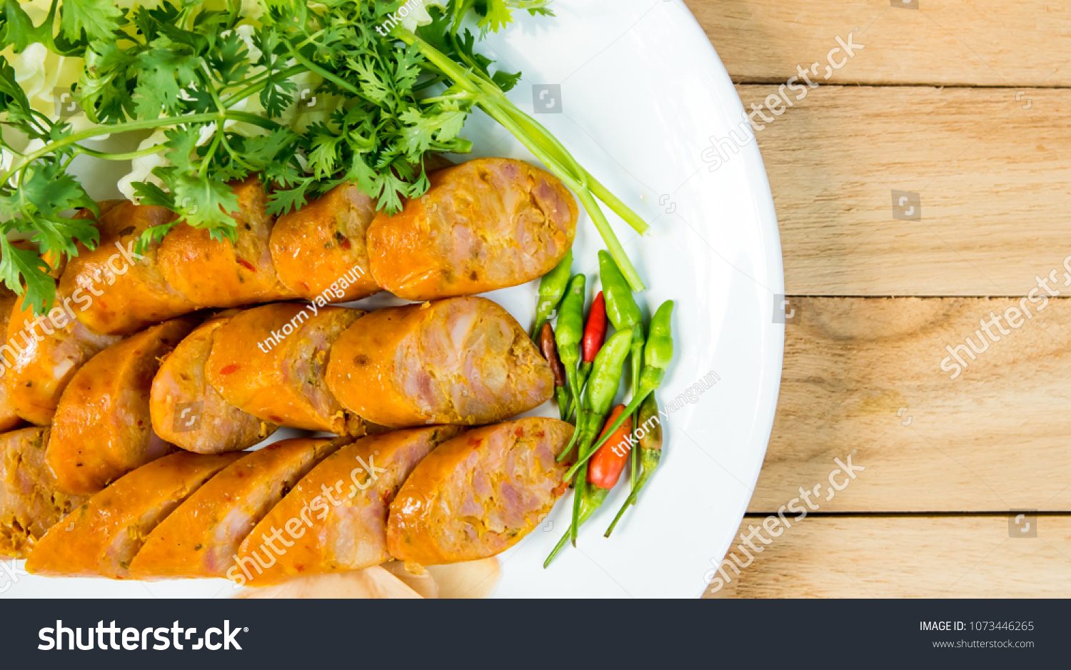 Close up Thai sausage with ginger, chilli and coriander on white plate on  wooden table. #1073446265