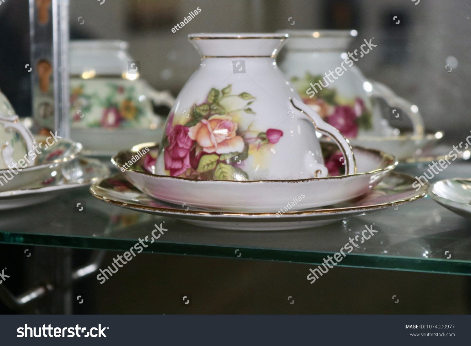 Antique and vintage floral bone china teacups and saucers through clear glass cabinet with blurred background #1074000977