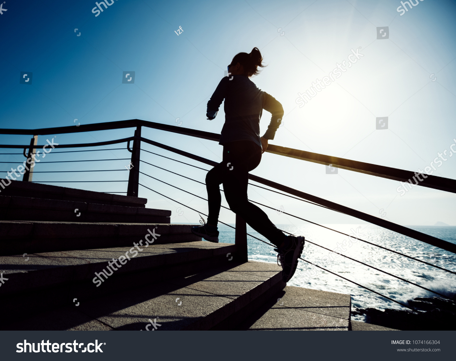 sporty female runner running upstairs on coast trail #1074166304