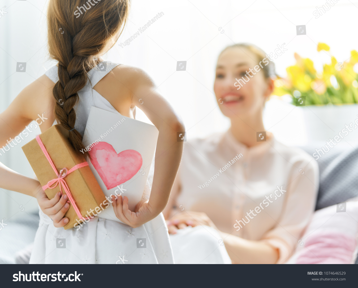 Happy women's day! Child daughter is congratulating mom and giving her postcard and gift. Mum and girl smiling and hugging. Family holiday and togetherness. #1074646529