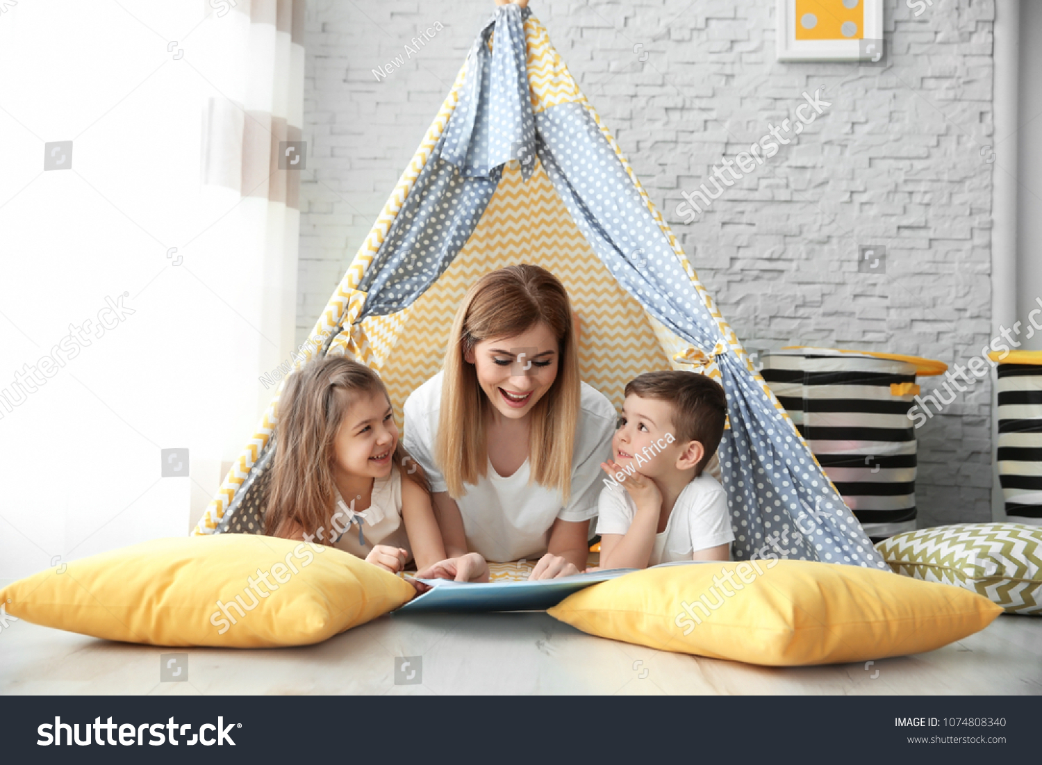 Nanny and little children reading book in tent at home #1074808340