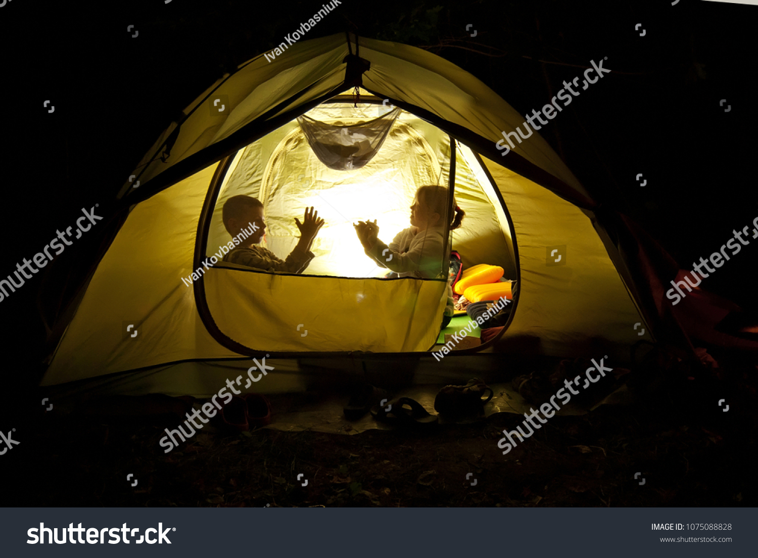 children play in the hike. the tent lights at night from the flashlight. dark silhouettes of children. #1075088828