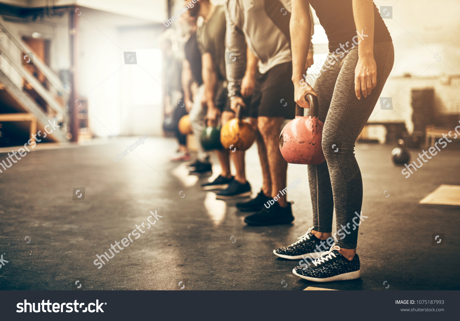 Fit group people in exercise gear standing in a row holding dumbbells during an exercise class at the gym #1075187993