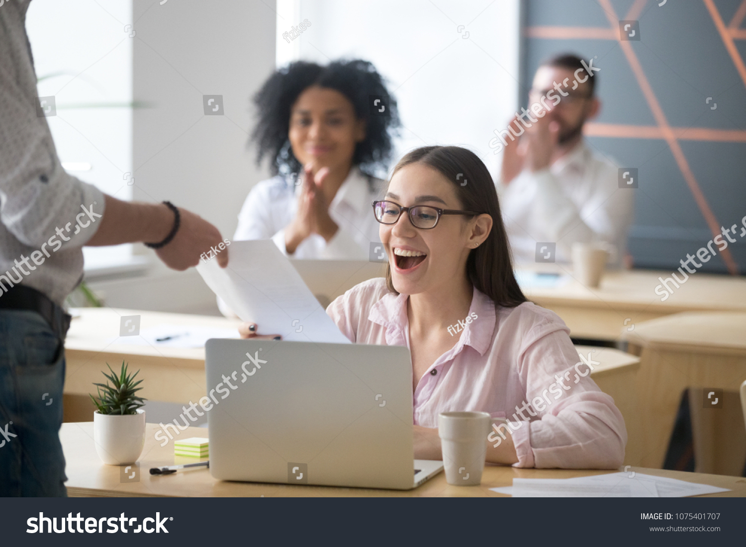 Excited successful student receiving document from boss with good result, colleagues congratulating happy millennial promoted rewarded employee amazed by great news in written notice with applause #1075401707