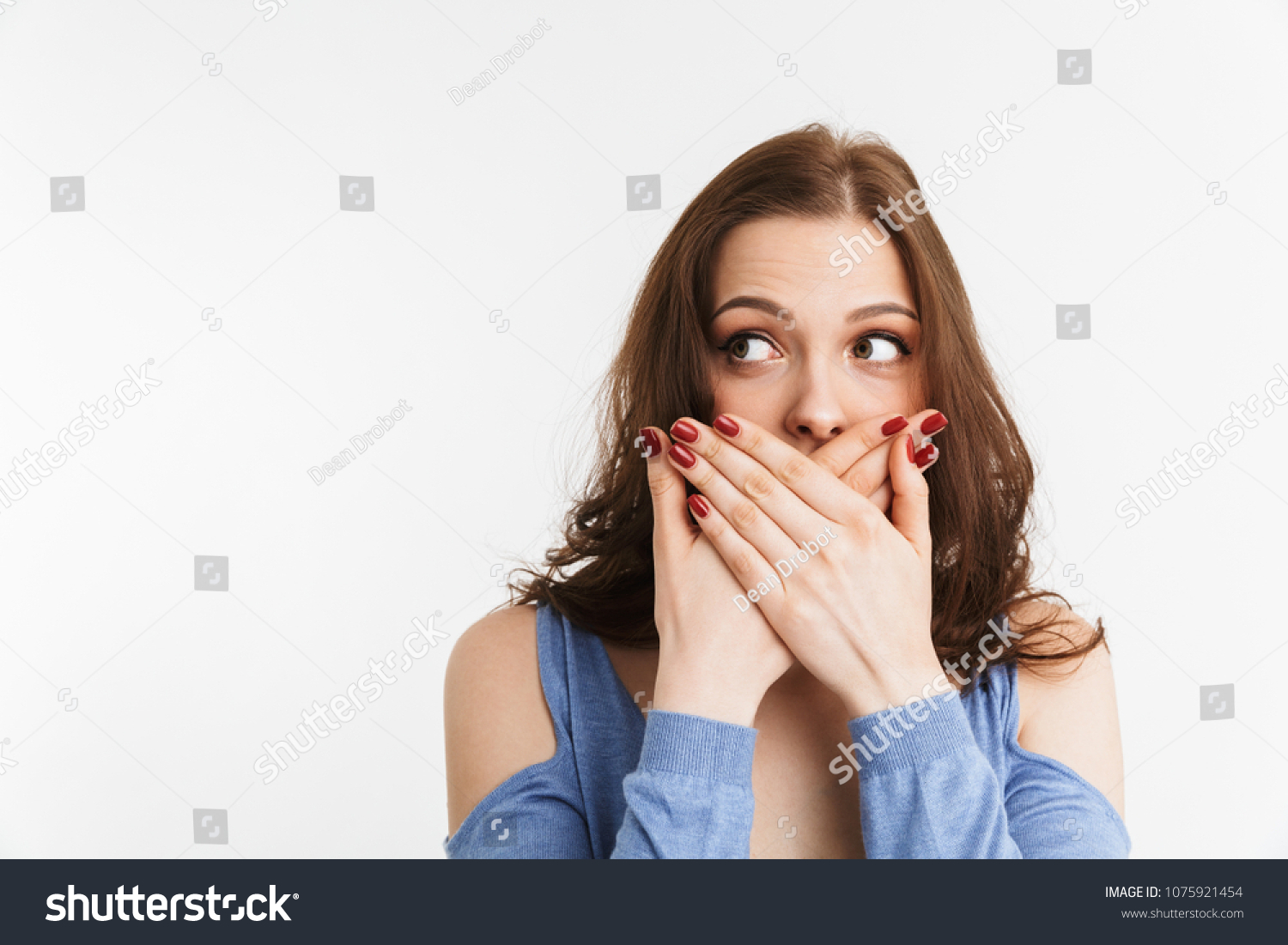Portrait of a surprised young woman covering mouth with hands isolated over white background #1075921454