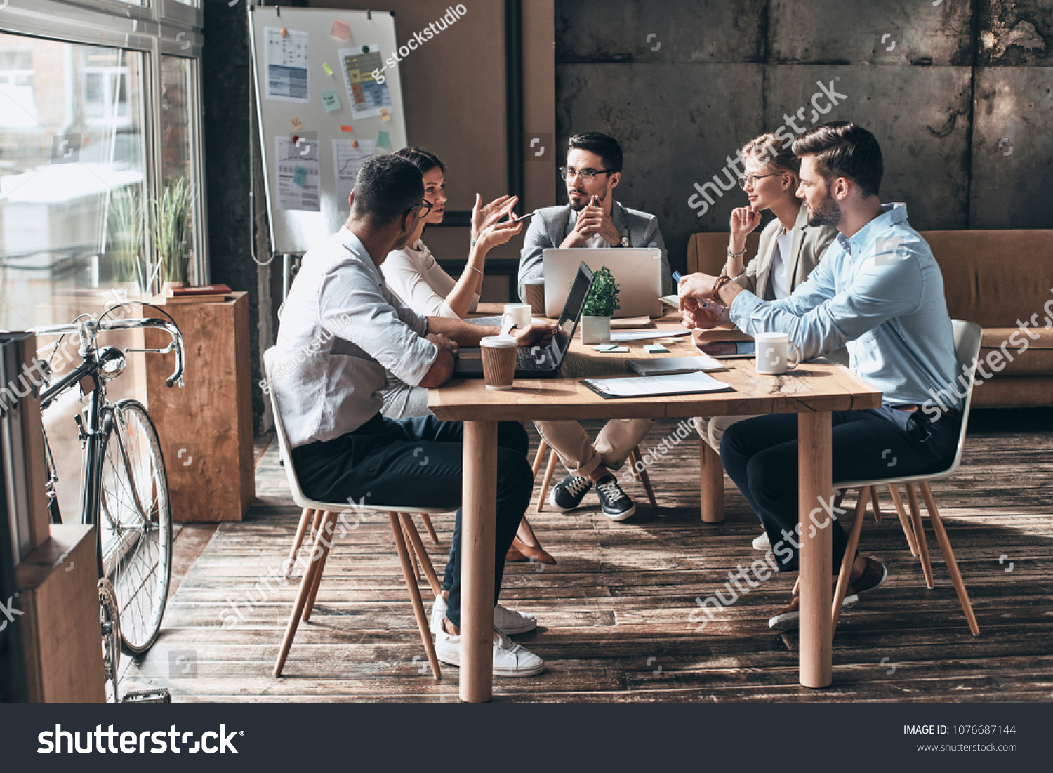 Confident and successful team. Group of young modern people in smart casual wear discussing business while sitting in the creative office #1076687144