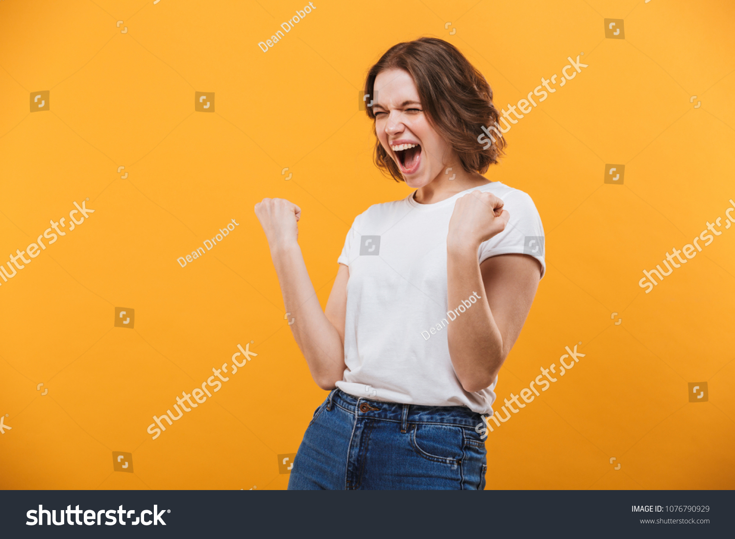 Image of excited young woman standing isolated over yellow background make winner gesture. #1076790929