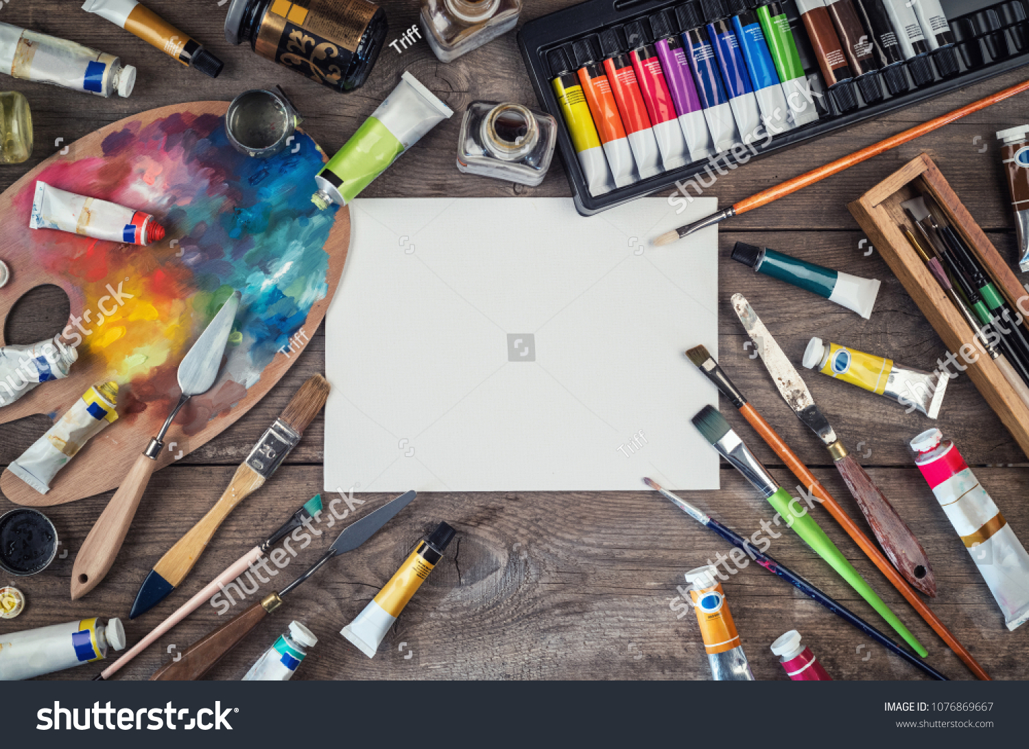 Set of artist accessories collection. Canvas, tube of oil paint, art brushes, palette knife lying on the wood table. Artist workshop background. #1076869667
