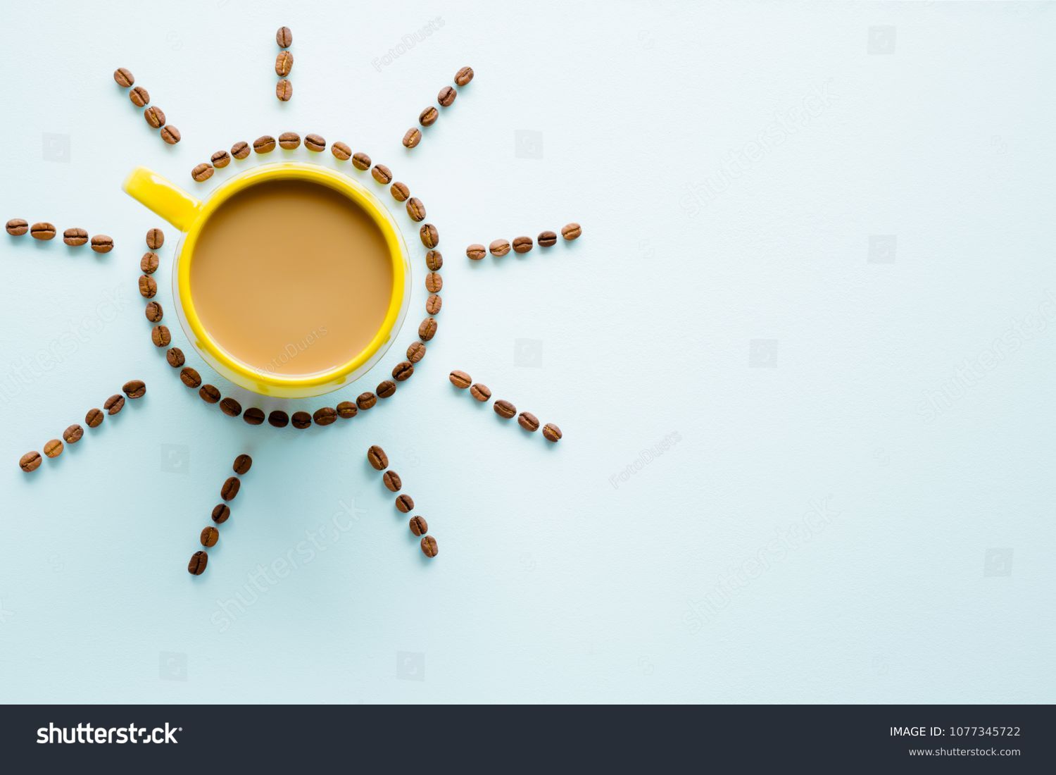 Yellow mug of coffee with milk on light pastel blue table from above. Wake up with morning coffee. Sun created from brown beans. Empty place for inspirational, motivational text or quote.  Top view. #1077345722