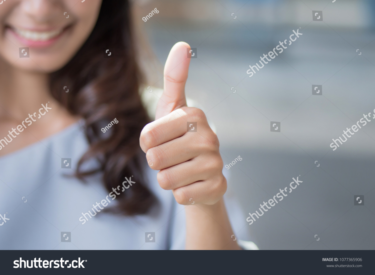 successful girl pointing thumb up sign gesture; portrait of cheerful smiling woman pointing up approving, yes, ok, good, thumb up gesture; asian woman young adult model #1077365906