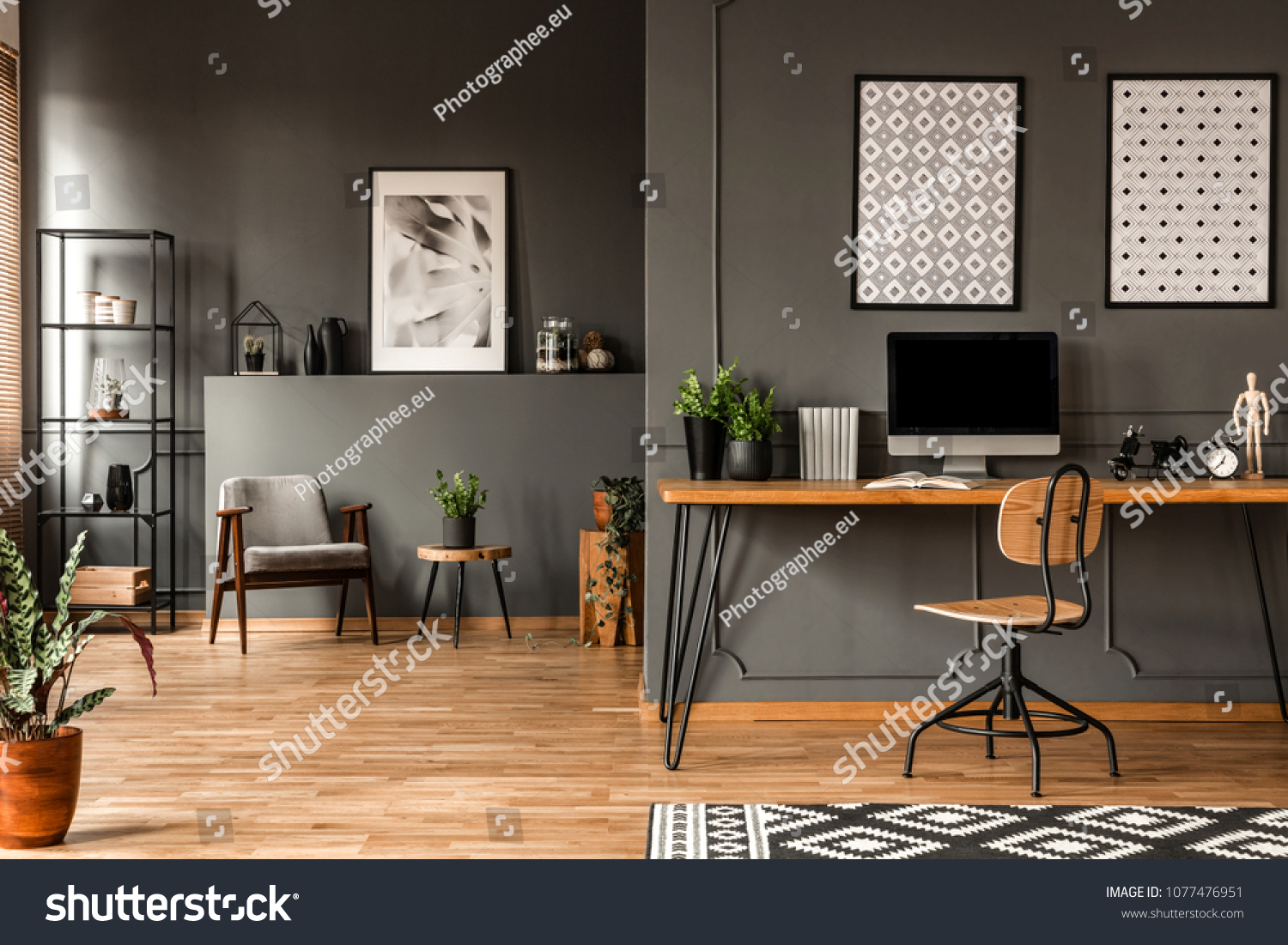 Patterned posters above desk with computer monitor in grey home office interior with plants #1077476951